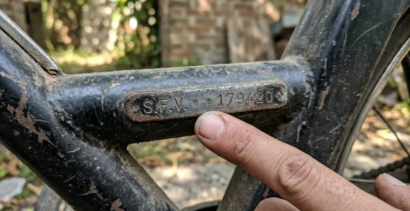 Un doigt pointe vers des chiffres gravés sur le cadre métallique d'un cyclomoteur ancien à l'extérieur